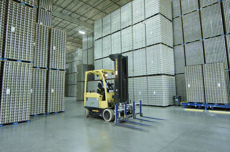 Forklift moving stacked pallets of manufactured cans in a Silgan Containers warehouse